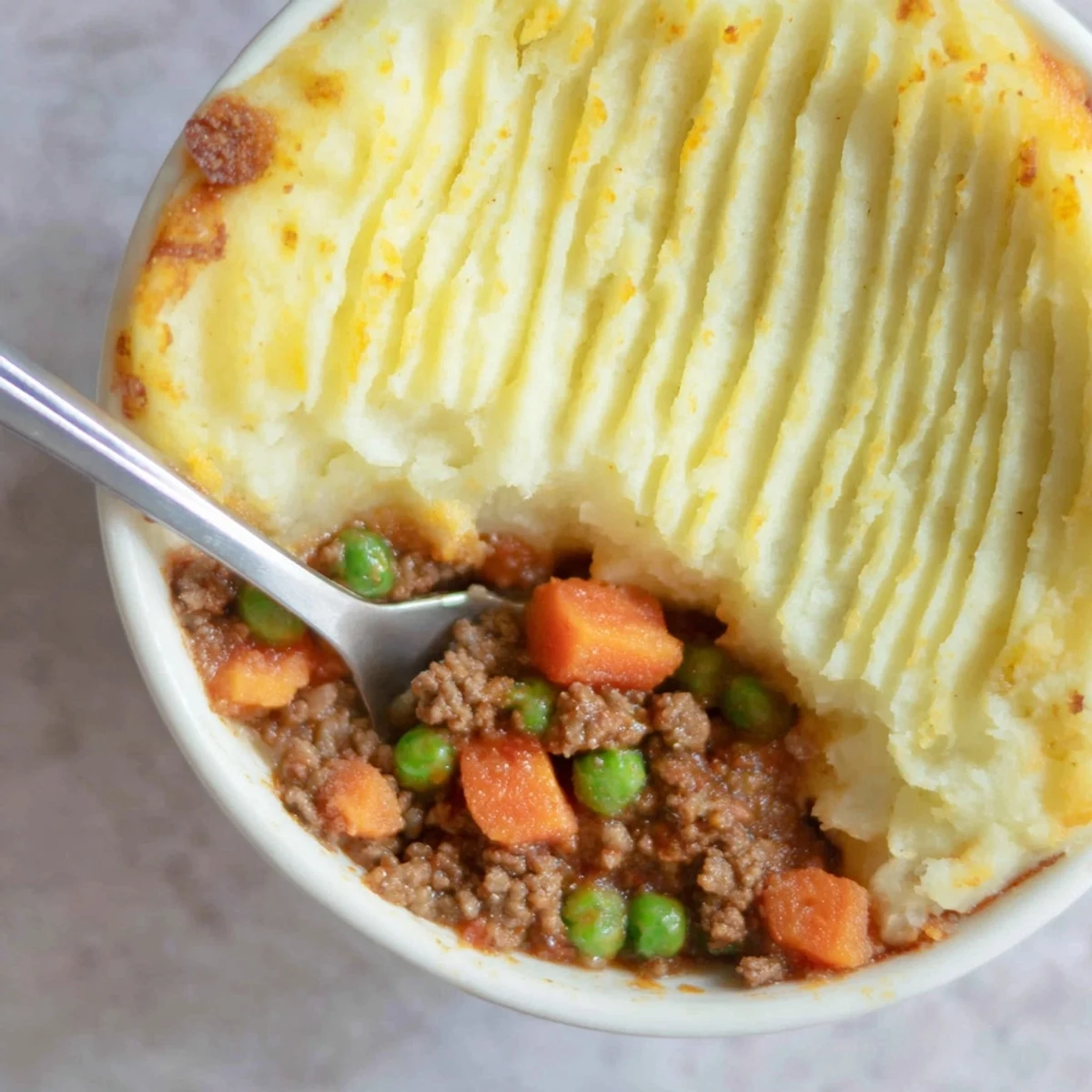 Golden brown mashed potatoes cover a bubbling dish of Beef Shepherds Pie with Peas and savory ground beef.